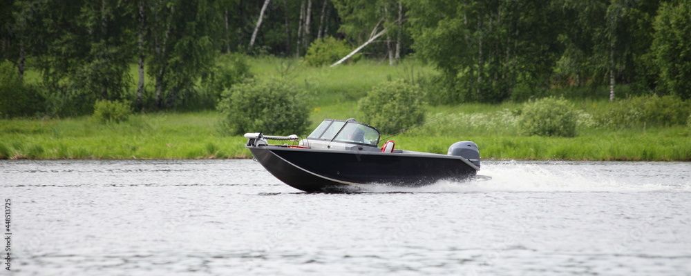 Fast gliding Russian fishing motor boat side view on green trees on far shore background in Tver ragion at summer day, active recreation boating tourism on Volga river