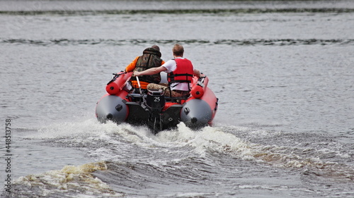 Two man in red lifejackets on red inflatable motor boat with powerful outboard motor fast floating on the river water , outdoor active recreation at summer day