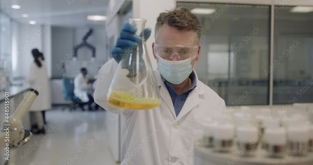 Male scientist looking at conical flask sample in a laboratory Male scientist looking at conical flask sample in a laboratory