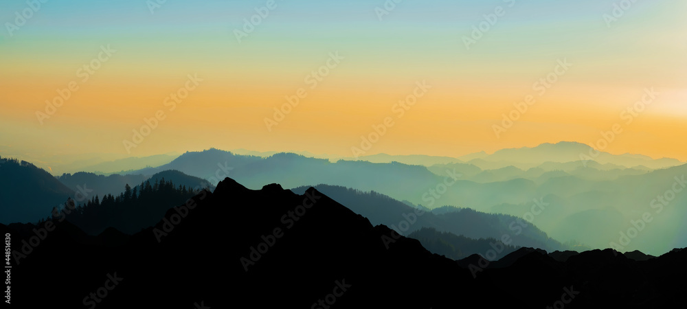 Landscape background banner panorama -.Breathtaking view with black silhouette of mountains, hills and forest, in the evening during the sunset, with a brightly colored sky