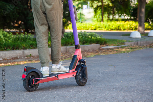 Close-up of the legs of a young man on an electronic scooter against the background of asphalt in city park