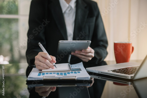 Businesswomen use tablet and laptop computer and take notes in the notebook at the office desk in the morning.
