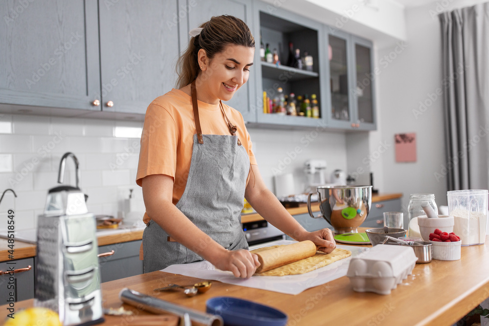 culinary, bake and people concept - happy smiling young woman cooking food on kitchen at home rolls dough with rolling pin culinary, bake and people concept - happy smiling young woman cooking food on kitchen at home rolls dough with rolling pin