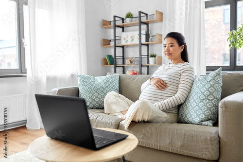 pregnancy, rest, people and expectation concept - pregnant asian woman with laptop computer sitting on sofa at home