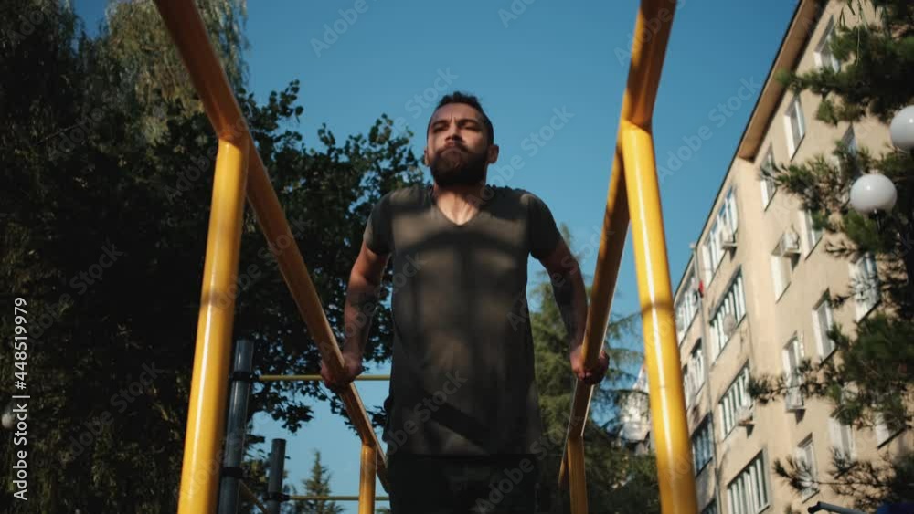 Caucasian man with beard and dreadlocks does push ups on parallel bars outside. Sports activities on outdoor ground and healthy lifestyle. Fitness and strength exercises for muscles of arms. Caucasian man with beard and dreadlocks does push ups on parallel bars outside. Sports activities on outdoor ground and healthy lifestyle. Fitness and strength exercises for muscles of arms.