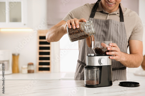 Man using electric coffee grinder in kitchen, closeup