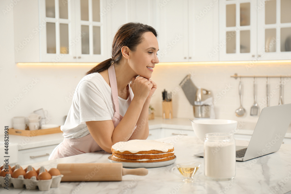 Woman making cake while watching online cooking course via laptop in kitchen Woman making cake while watching online cooking course via laptop in kitchen