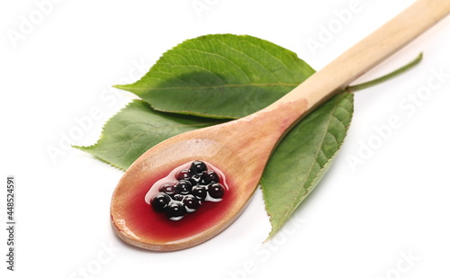 Squeezed elderberries juice, syrup in wooden spoon with elder berries and leaves isolated on white background