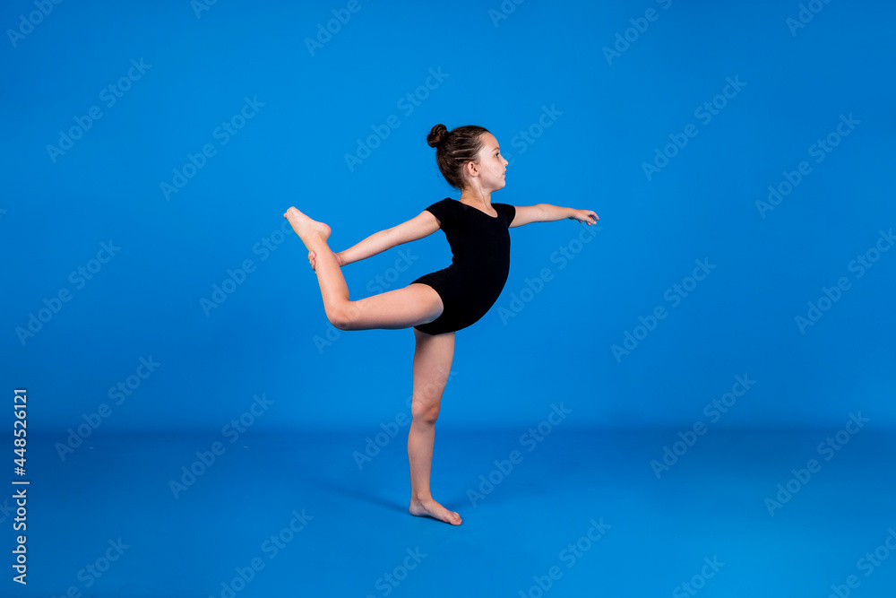 a small gymnast in a black swimsuit performs flexibility exercises on a blue background with a place for text a small gymnast in a black swimsuit performs flexibility exercises on a blue background with a place for text