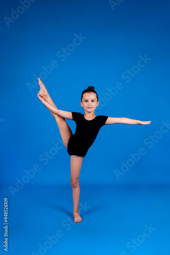 a little girl in a black swimsuit performs stretching exercises on a blue background with a place for text