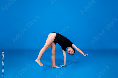 a little girl in a black swimsuit performs a wheel exercise on a blue background with a place for text