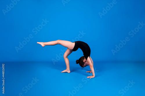 a little girl in a black swimsuit performs a rhythmic gymnastics exercise on a blue background with a place for text