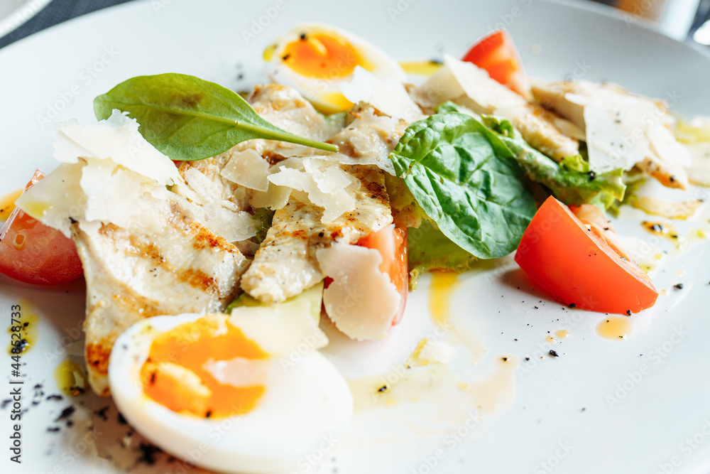 Classical Caesar salad with roasted chiken, eggs, lettuce leaves, parmesan and cherry tomatoes on the white plate close up Classical Caesar salad with roasted chiken, eggs, lettuce leaves, parmesan and cherry tomatoes on the white plate close up