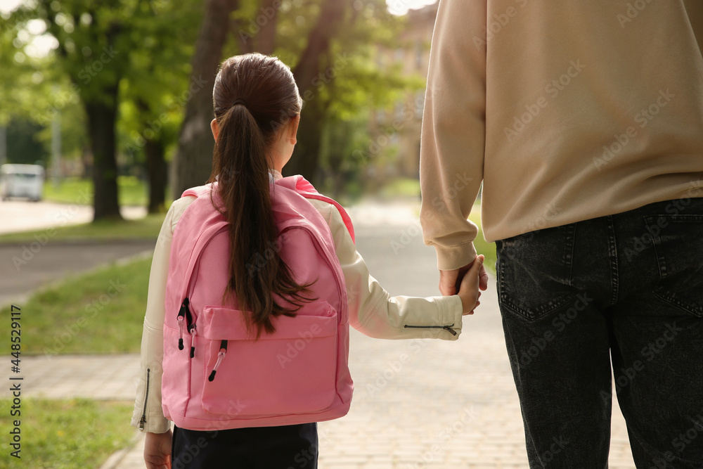 Fototapeta premium Father taking his little daughter to school through park, back view