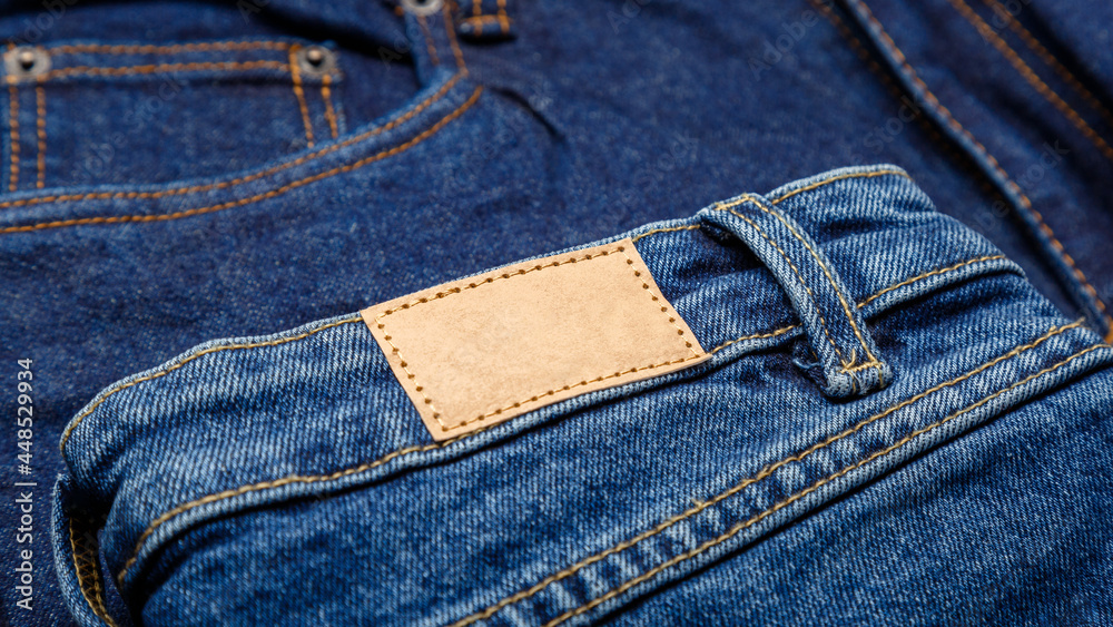Blue denim jeans with emty label. Brown blank leather label tag on denim pants background. Blank mockup beige leather label. Close up long web banner