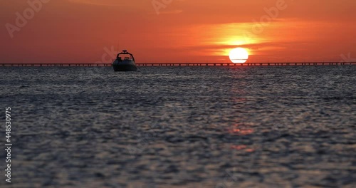 Beautiful sunset behind the Chesapeake Bay Bridge Tunnel with boat at anchor in foreground. Slow motion view of gentle waves and calm surface reflecting evening sun on water. Peaceful ocean paradise. photo