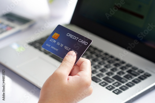 Female hand holding credit card and laptop computer on white desk. Concept of Online shopping and payment.