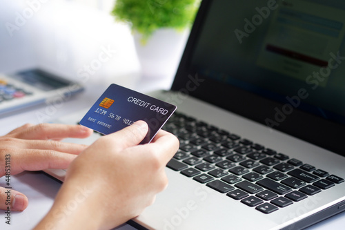 Female hand holding credit card and laptop computer on white desk. Concept of Online shopping and payment.