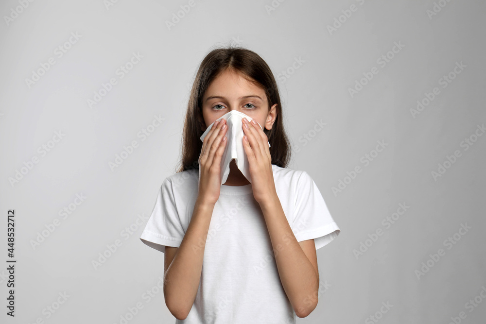 Little girl blowing nose into paper tissue on light grey background. Seasonal allergy Little girl blowing nose into paper tissue on light grey background. Seasonal allergy