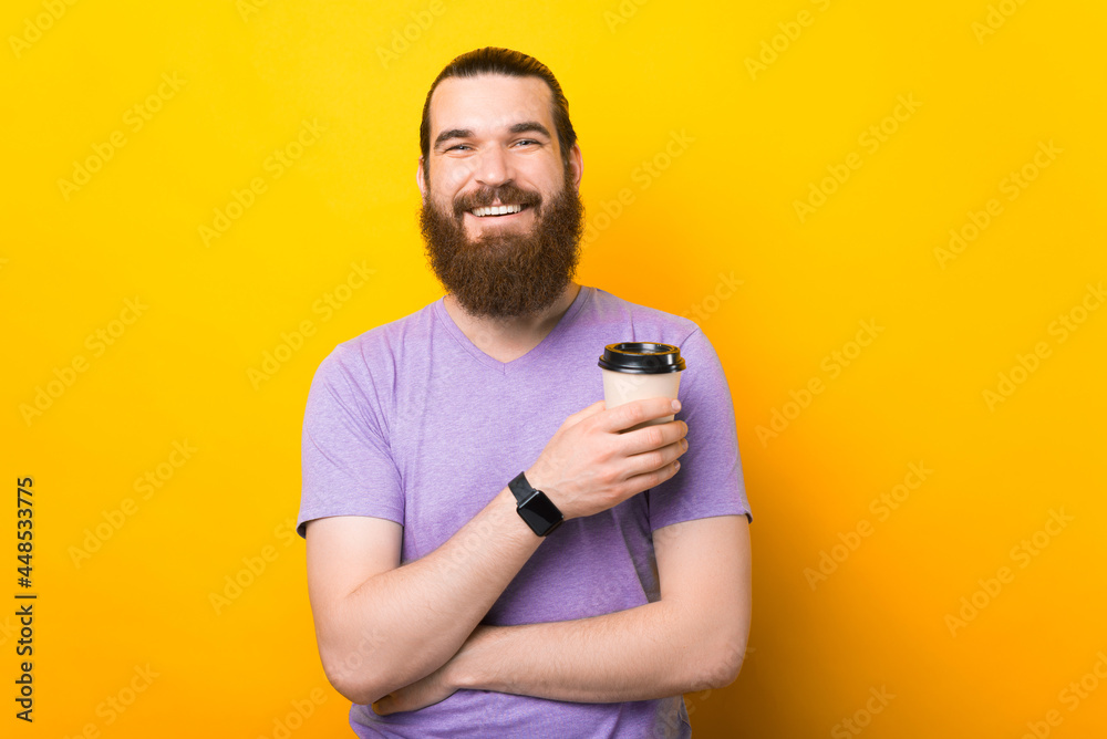 Bearded man on vibrant yellow color holding hot coffee in takeaway paper cup Bearded man on vibrant yellow color holding hot coffee in takeaway paper cup