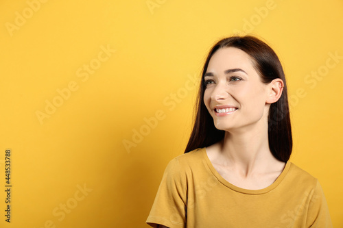 Portrait of pretty young woman with gorgeous chestnut hair and charming smile on yellow background, space for text