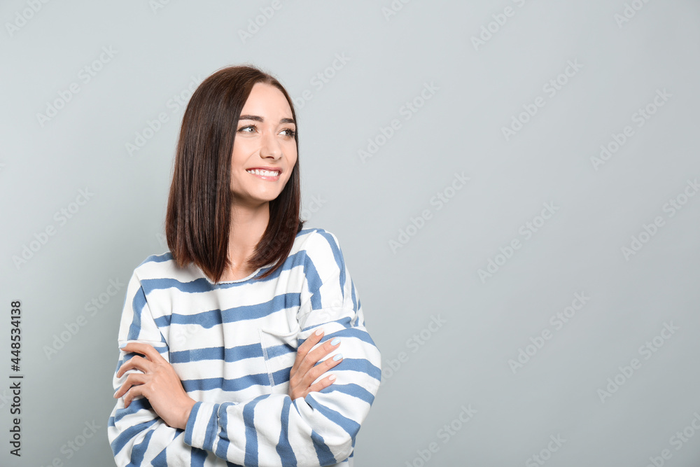 Portrait of pretty young woman with gorgeous chestnut hair and charming smile on light grey background, space for text Portrait of pretty young woman with gorgeous chestnut hair and charming smile on light grey background, space for text