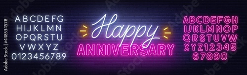 Happy anniversary neon text. Greeting card on brick wall background. Pink and white neon alphabets.