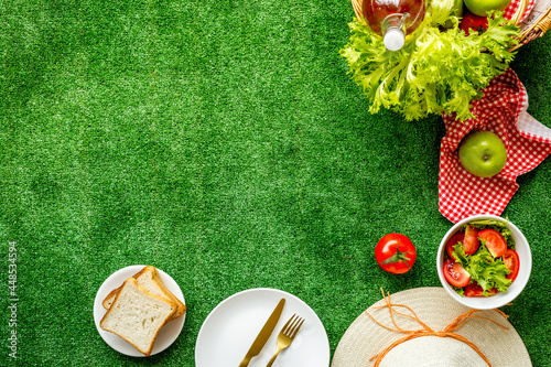Picnic setting on meadow with basket and food on red cloth. Overhead view