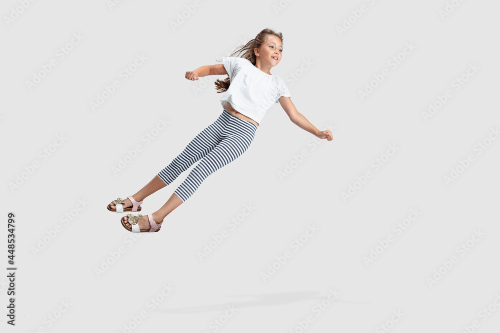 Full-length portrait of beautiful little girl falling down isolated on gray studio background. Childhood, education, emotion concept. Flyer