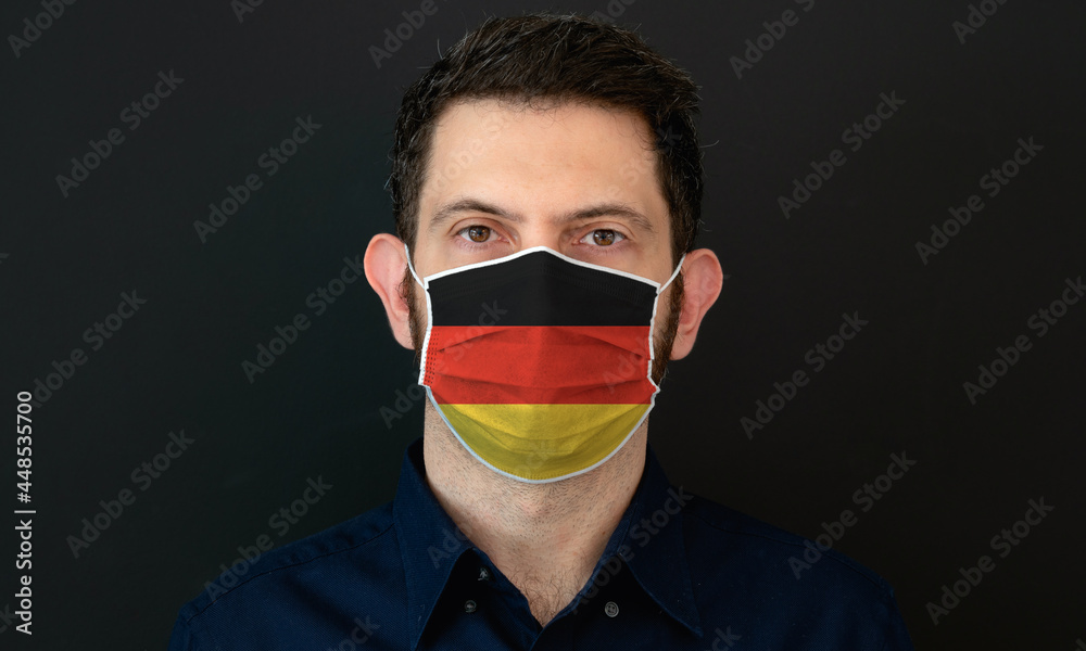 Man wearing German flag protective medical face mask. He looks worried and concerned. Coronavirus concept in Germany with black background. Man wearing German flag protective medical face mask. He looks worried and concerned. Coronavirus concept in Germany with black background.