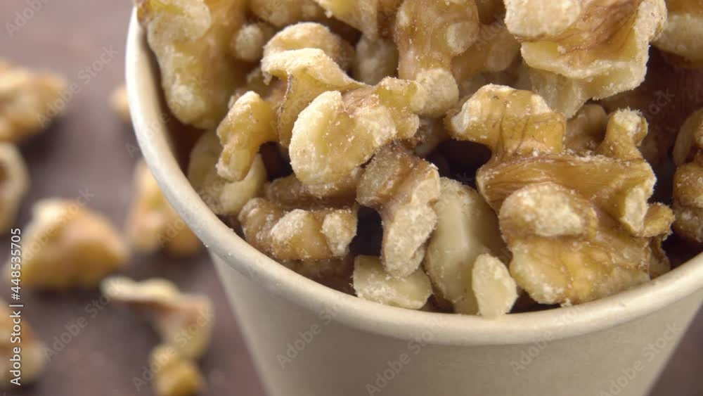 Peeled walnuts in a full paper cup on a rotating wooden surface. Macro. Selective focus. Vitamin fatty snack. Peeled walnuts in a full paper cup on a rotating wooden surface. Macro. Selective focus. Vitamin fatty snack.