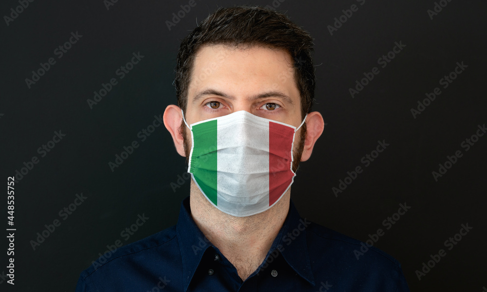 Man wearing Italian flag protective medical face mask. He looks worried and concerned. Coronavirus concept in Italy with black background. Man wearing Italian flag protective medical face mask. He looks worried and concerned. Coronavirus concept in Italy with black background.