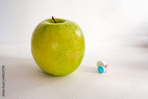Green apple or vitamin pills on a white background. Healthy eating, diet, lifestyle concept, treatment choice concept