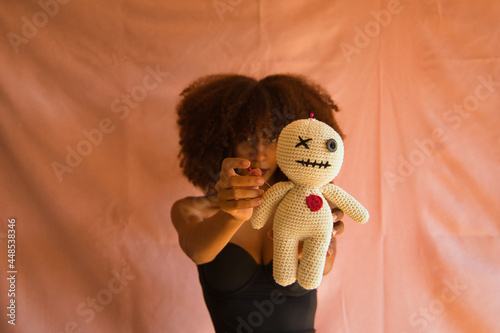 Obraz na plátne Young Latina woman in black dress holding voodoo doll in foreground on pink background