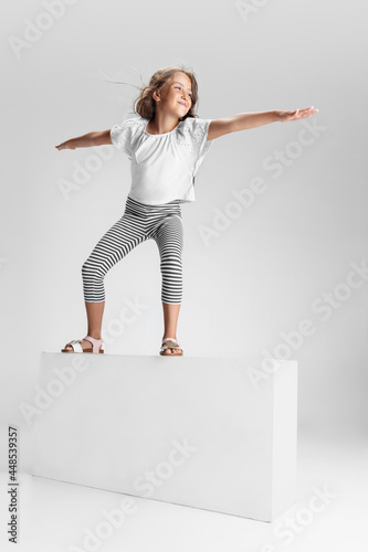 Caucasian preschool girl standing on big box isolated over white studio background. Copyspace. Childhood, education, emotions concept