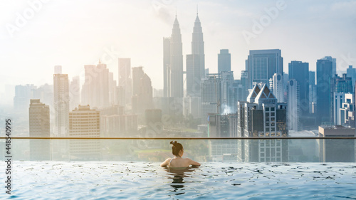 Photography young Asian woman enjoying in hotel roof top swimming pool, city view with blue
