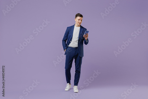Full size young successful employee business man lawyer 20s wear formal blue suit white t-shirt move stroll hold use mobile cell phone hand in pocket isolated pastel purple background studio portrait.