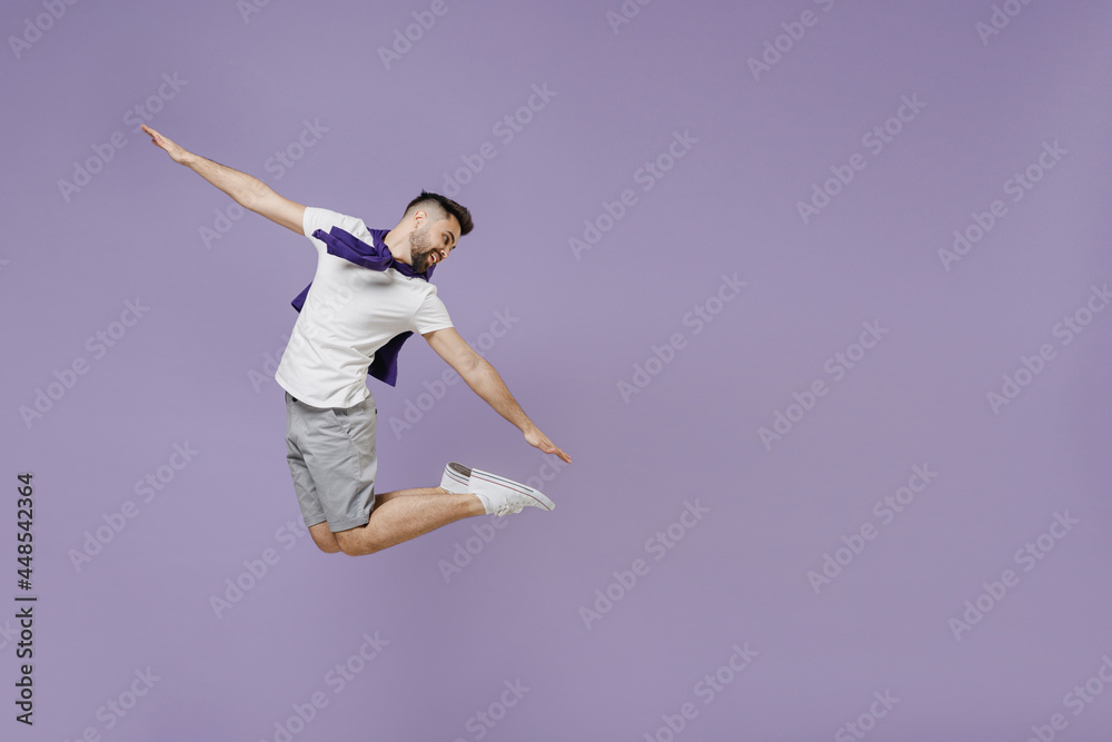 Full size body length happy fun young brunet man 20s wear white t-shirt purple shirt jump like flying look back isolated on pastel violet background studio portrait. People emotions lifestyle concept.