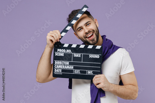 Pampering loony charming fun young brunet man 20s wear white t-shirt purple shirt holding classic black film making hiding behind it clapperboard isolated on pastel violet background studio portrait © ViDi Studio