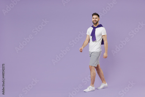 Full size body length happy fun young brunet man 20s wear white t-shirt purple shirt go step walk pace stroll isolated on pastel violet background studio portrait. People emotions lifestyle concept © ViDi Studio