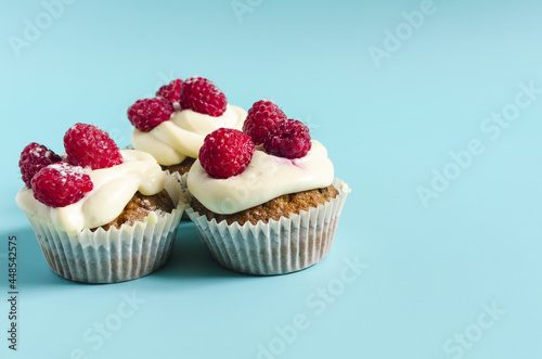 Homemade cupcakes with white cream and berries on a blue background. Sweet cupcakes on a colored background are a place for text.