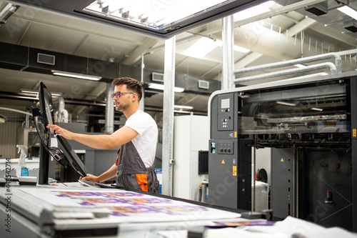Print house worker setting parameters on modern offset printing machine.
