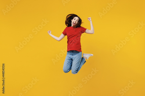 Full size body length excited young brunette woman 20s wears basic red t-shirt jump doing winner gesture celebrating isolated on yellow background studio portrait. People emotions lifestyle concept © ViDi Studio