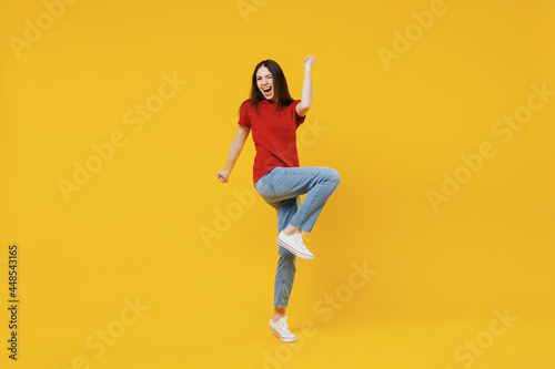 Full size body length happy excited young brunette woman 20s wears basic red t-shirt doing winner gesture celebrating isolated on yellow background studio portrait. People emotions lifestyle concept.
