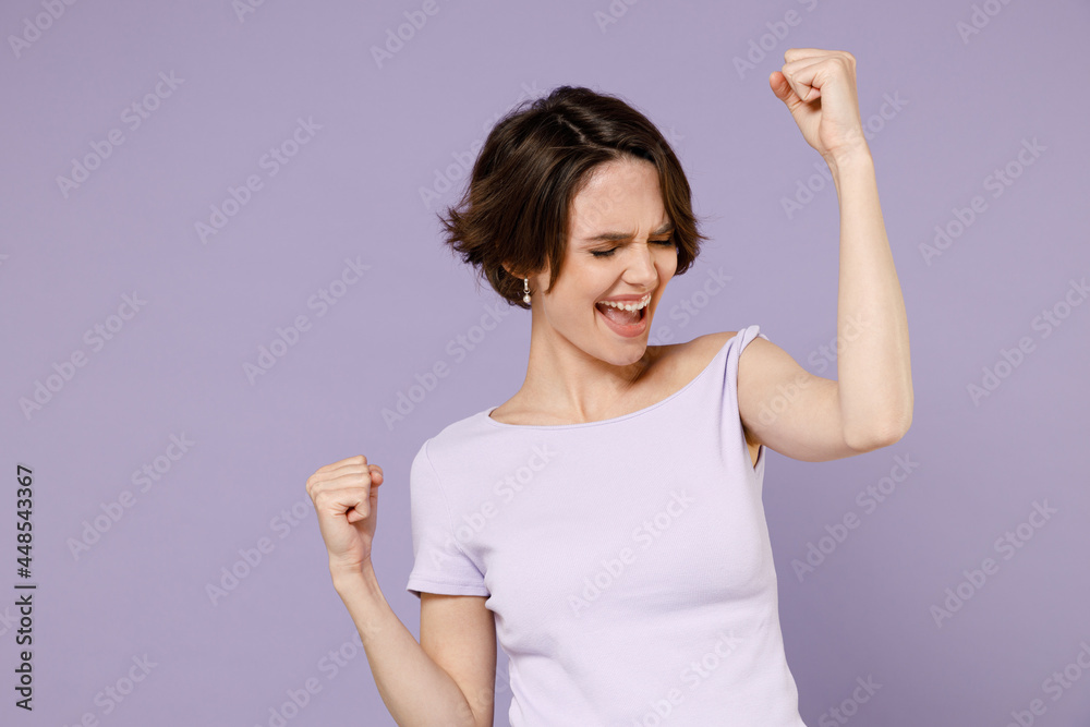 Young overjoyed happy brunette woman 20s with bob haircut wearing white t-shirt do winner gesture clench fist say yes isolated on pastel purple background studio portrait. People lifestyle concept Young overjoyed happy brunette woman 20s with bob haircut wearing white t-shirt do winner gesture clench fist say yes isolated on pastel purple background studio portrait. People lifestyle concept