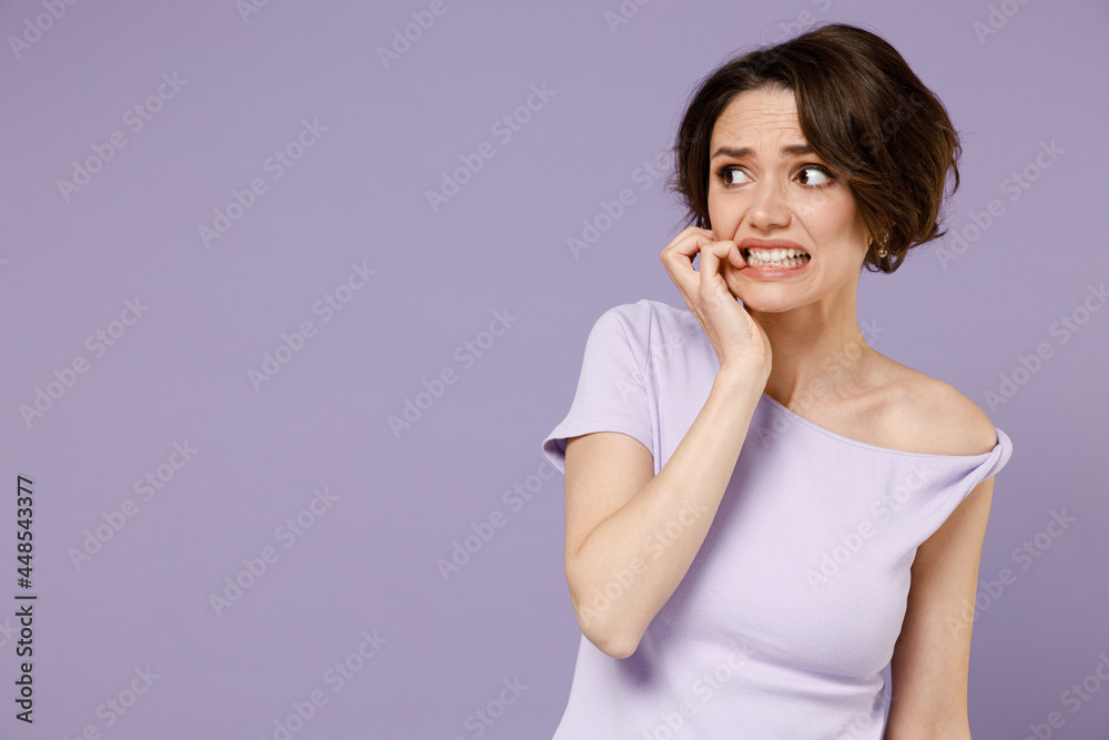 Young disappointed puzzled confused embarrassed woman 20s with bob haircut wear white t-shirt look aside biting nails isolated on pastel purple background studio portrait People lifestyle concept. Young disappointed puzzled confused embarrassed woman 20s with bob haircut wear white t-shirt look aside biting nails isolated on pastel purple background studio portrait People lifestyle concept.