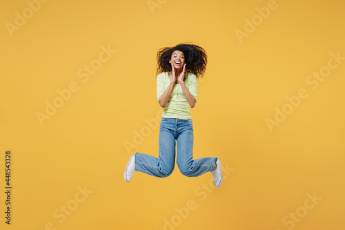 Full size body length shocked african american young woman 20s wears green shirt keep mouth wide open look surprised isolated on yellow background studio portrait. People emotions lifestyle concept