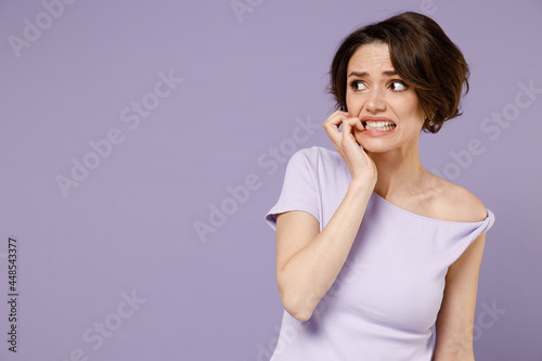 Young disappointed puzzled confused embarrassed woman 20s with bob haircut wear white t-shirt look aside biting nails isolated on pastel purple background studio portrait People lifestyle concept.