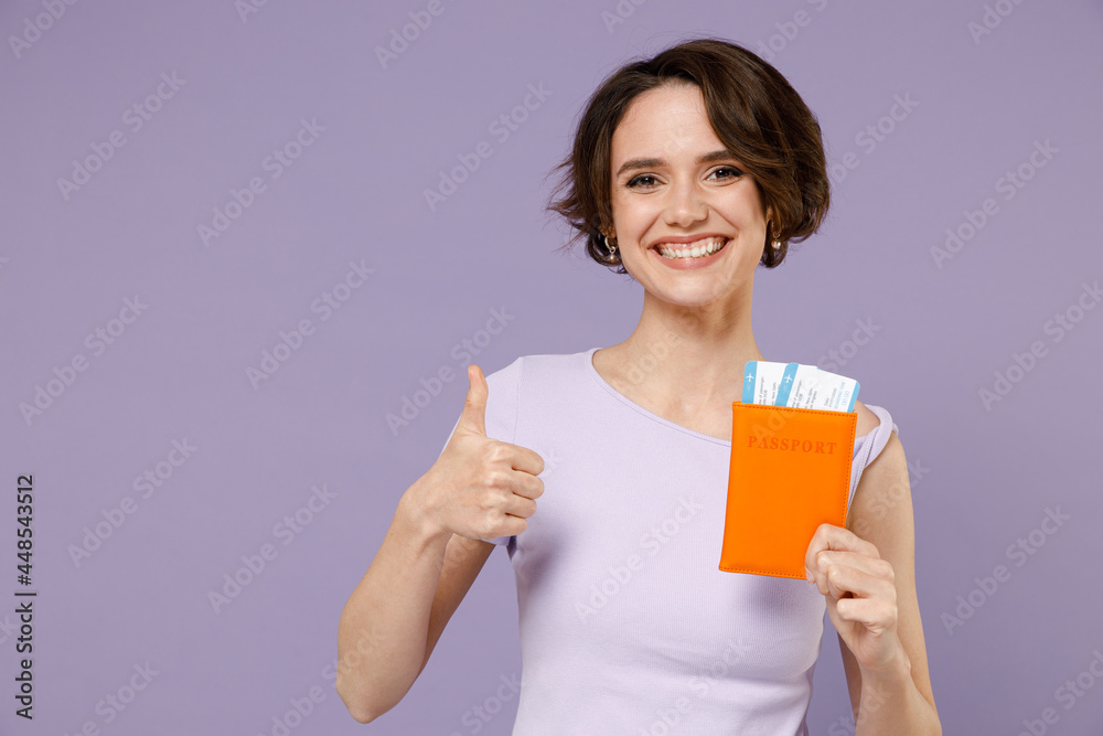 Traveler tourist woman in white t-shirt hold passport boarding tickets show thumb up gesture isolated on pastel purple background studio Passenger travel abroad weekends getaway. Air flight concept. Traveler tourist woman in white t-shirt hold passport boarding tickets show thumb up gesture isolated on pastel purple background studio Passenger travel abroad weekends getaway. Air flight concept.