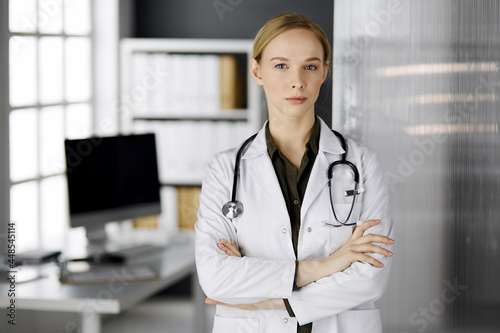 Friendly smiling female doctor standing in clinic. Portrait of friendly physician woman. Perfect medical service in hospital